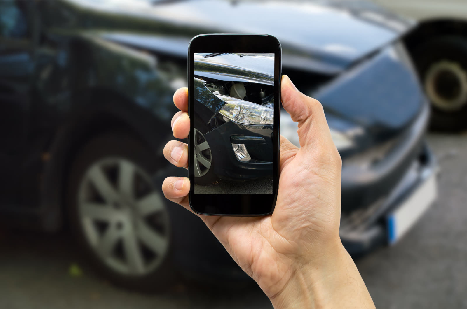 Une main photographie avec un smartphone les dégâts sur la carrosserie d’une voiture.